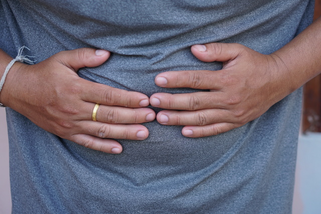 Man with Hands on Stomach Indicative of Discomfort or Pain in Casual Grey Shirt Background Close-Up