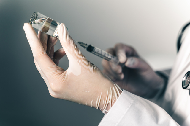 The doctor holding a syringe with Covid-19 vaccines in glass bot
