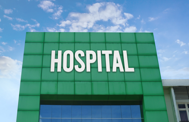 Modern green facade with a large HOSPITAL sign against a cloudy blue sky.