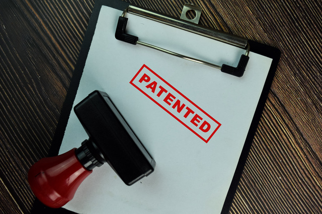 Red Handle Rubber Stamper and Patented text isolated on Wooden Table.